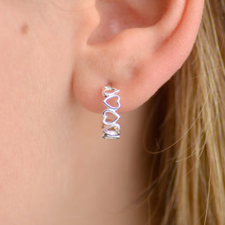 Silver open heart hoop earrings shown close up on model