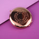 Rose gold compact mirror with personalised spiral message engraved on the front, shown in close up shot on purple background.