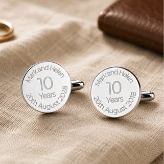 Silver cufflinks with engraved text on a beige fabric background