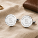 Silver cufflinks with engraved text on a beige fabric background