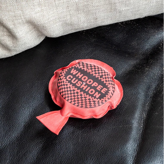 Red whoppee cushion on a black leather surface with a gray fabric background