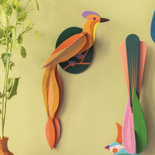 Colorful bird-shaped wall decorations on a light green wall with a vase of flowers.