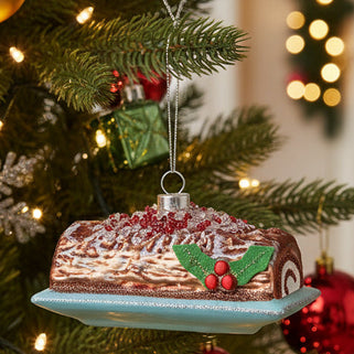 A holiday ornament depicting a chocolate roll with a Christmas tree on top, surrounded by glitter and red accents.