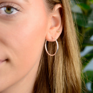Sterling silver medium sized hoop earrings shown in close up shot on model.