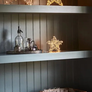Decorative star lights on a shelf against a wooden panel wall.