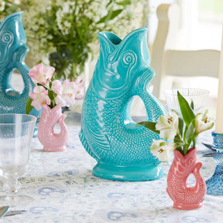 Turquoise and pink fish-shaped vases on a table with floral arrangements.