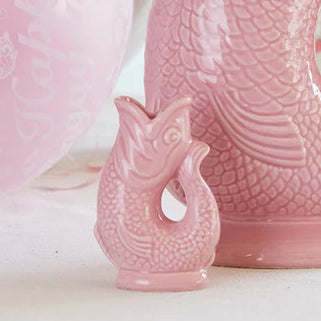 Pink ceramic vase with floral arrangement on a table with glasses and decorative items.