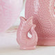 Pink ceramic vase with floral arrangement on a table with glasses and decorative items.