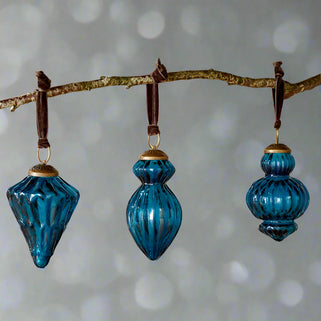Three blue glass ornaments hanging from a branch against a light background