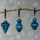 Three blue glass ornaments hanging from a branch against a light background
