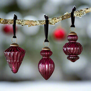 Three red glass ornaments hanging from a branch with a soft background