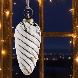 Two decorative cone-shaped ornaments with wavy pattern hanging against a beige background with string lights.