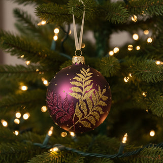 A purple and gold glittery glass bauble with a fern leaf design, intended for hanging on a Christmas tree.