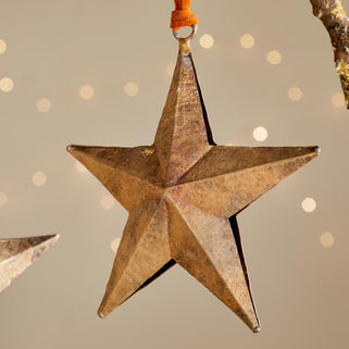Two rustic star-shaped ornaments hanging against a soft, blurred background with lights.