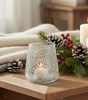 Cozy indoor setting with candles, pinecones, and a blanket on a wooden surface.