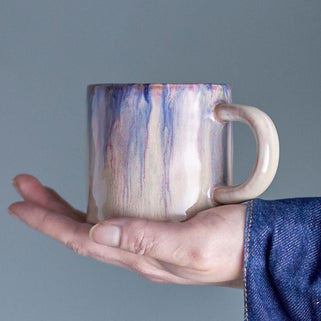 Hand holding a ceramic mug with a marbled design against a gray background