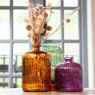 Three colorful glass vases with dried flowers on a windowsill.