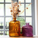 Three colorful glass vases with dried flowers on a windowsill.