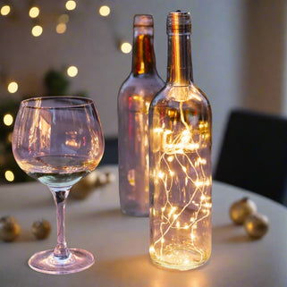 Wine bottle with string lights and wine glasses on a wooden table