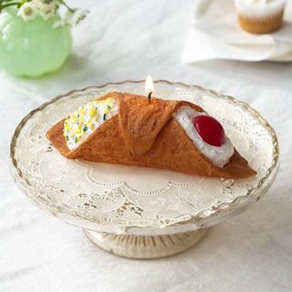 Crescent roll-shaped dessert with a candle on a lace cake stand.
