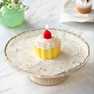 Small cake with a candle on a decorative plate with a vase of flowers in the background.