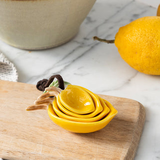 Yellow ceramic measuring cups on a wooden cutting board with lemons and a bowl in the background.