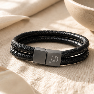 Black leather bracelet with a silver clasp on a beige fabric background