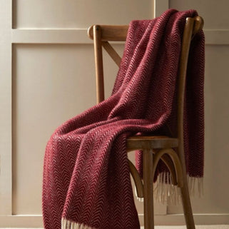 Burgundy wool throw blanket shown in lifestyle shot draped over wooden chair.