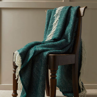 Teal patterned throw blanket draped over a wooden chair against a neutral wall.