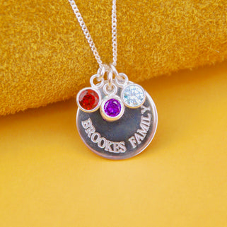 Personalised Family Names Birthstone Necklace - Silver engraved circle disc with "BROOKES FAMILY" and three birthstones  March/Aquamarine, July/Ruby, February/Amethyst shown close up