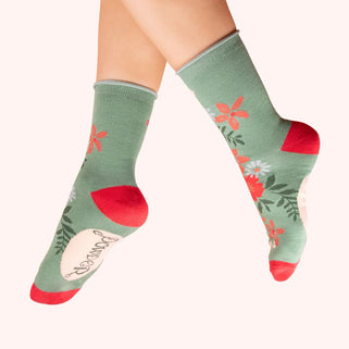 Green socks with floral patterns and red accents worn by a person on a white background