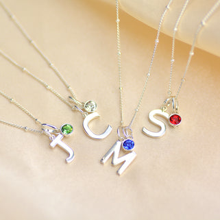 Modern initial and birthstone necklace shown colose up on satellite chain wih letter J, C, M and S and peridot, clear , ruby and sapphire birthstone charms