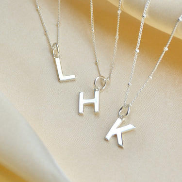 Modern Initial letter charm on satellite chain shown close up with letter L, H and K 