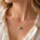 Gold necklace with three colorful gemstones worn by a person in a white shirt.