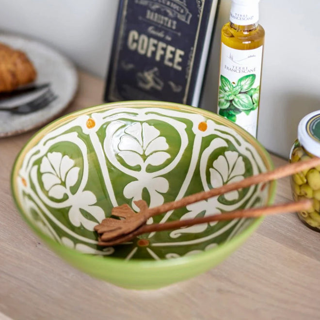 Decorative green bowl with white patterns on a table with a book and bottle in the background.