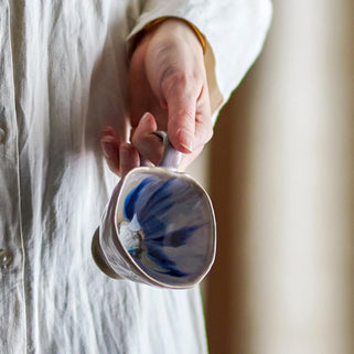 Person holding a ceramic mug with blue and white design against a neutral background