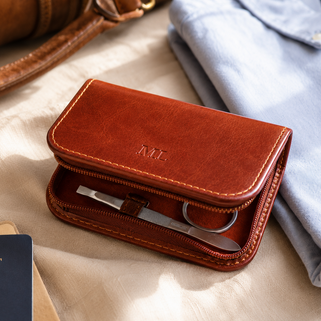 Brown leather wallet with 'ML' initials on a beige surface with a passport and clothing.