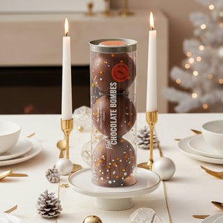 Tube of chocolate bombs with a single bomb open, revealing marshmallows on a white background