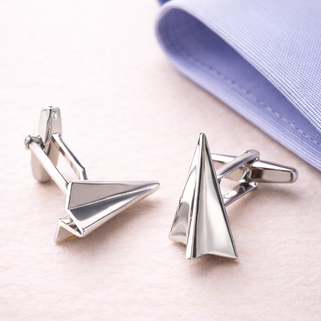Silver paper airplane cufflinks on a light pink background