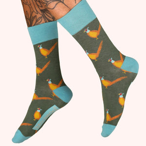 Socks with pheasant design on a green background, worn by a person with tattoos.