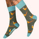 Socks with pheasant design on a green background, worn by a person with tattoos.