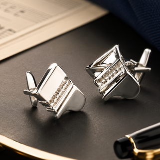 Silver cufflinks on a dark surface with a pen and paper in the background