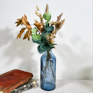 Blue glass bottle with dried flowers on a white surface