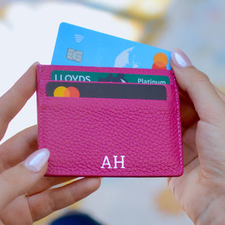 Pink cardholder with multiple cards inside, held by hands against a blurred background
