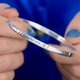 Sterling Silver Mia Hearts Bangle shown close up with model holding it. Hammered effect and brass hearts shown close up