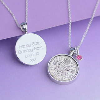 Personalised 1965 sixpence necklace with October/tourmaline birthstone, shown with engraving option on the back in straight walk font. Displayed in close up shot on purple background.