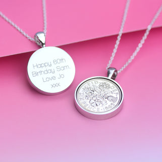 Personalised 1965 Sixpence Necklace with engraved message shown on the back in straight walk font. Shown in close up shot on pink background.