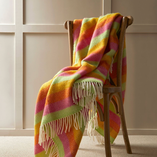 Pink, orange, yellow and green strip throw with diagonal texture detail, shown draped over chair in lifestyle shot.