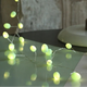 Warm white LED string lights with oval-shaped bulbs draped over a reflective surface, with a rustic stone wall in the background.
