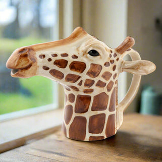 A beige and brown stoneware jug in the shape of a giraffe with a hand-painted design, featuring a spout for pouring.